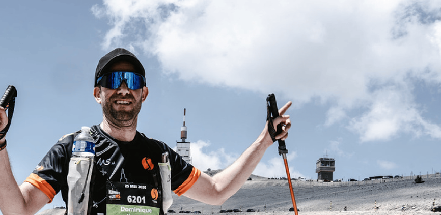 Dominique op de top van de Mont Ventoux, armen omhoog met de stokken in de lucht, in het shirt van Klimmen tegen MS.